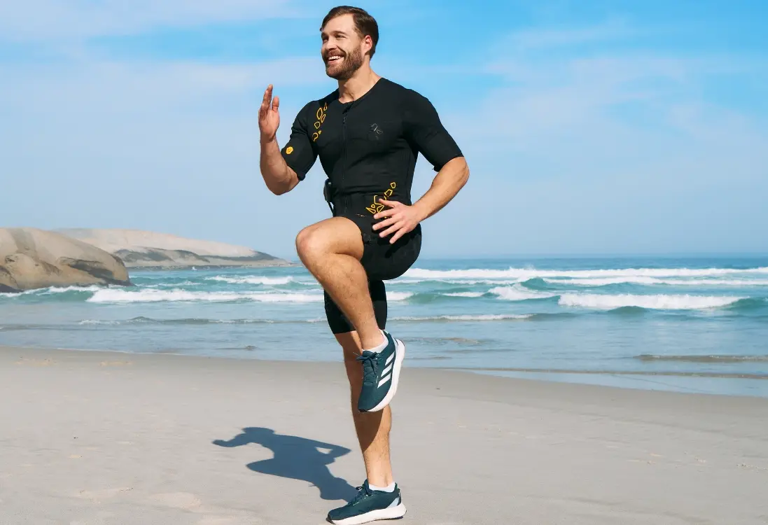 Afvallen met EMS - vetverliestraining in de buitenlucht Een man in een EMS-pak traint buiten op het strand en voert een effectieve en intensieve workout uit om vet te verminderen en gewichtsverlies te ondersteunen met EMS.